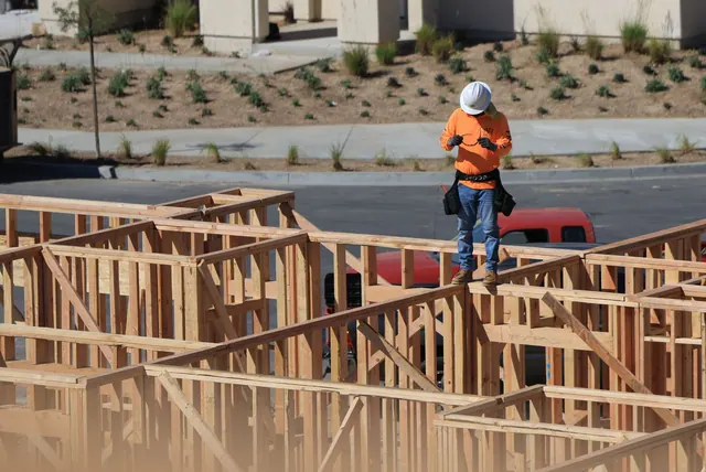 A construction worker on a wooden frame checks a device at a building site. Fence contractor hiring and training guide for 2027
