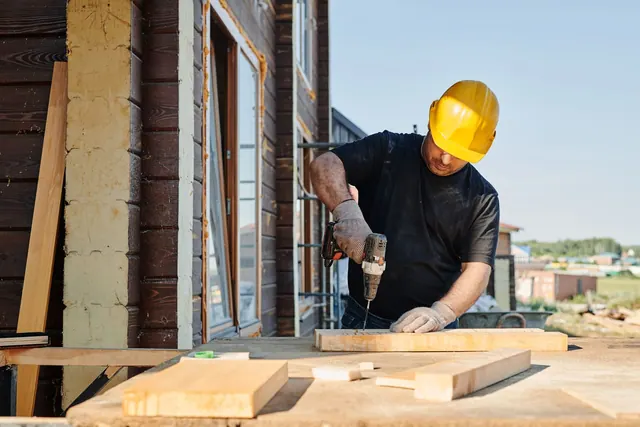 A construction worker using a power drill on a building site, outdoors during the day. Fence contractor pricing and profit guide for 2027
